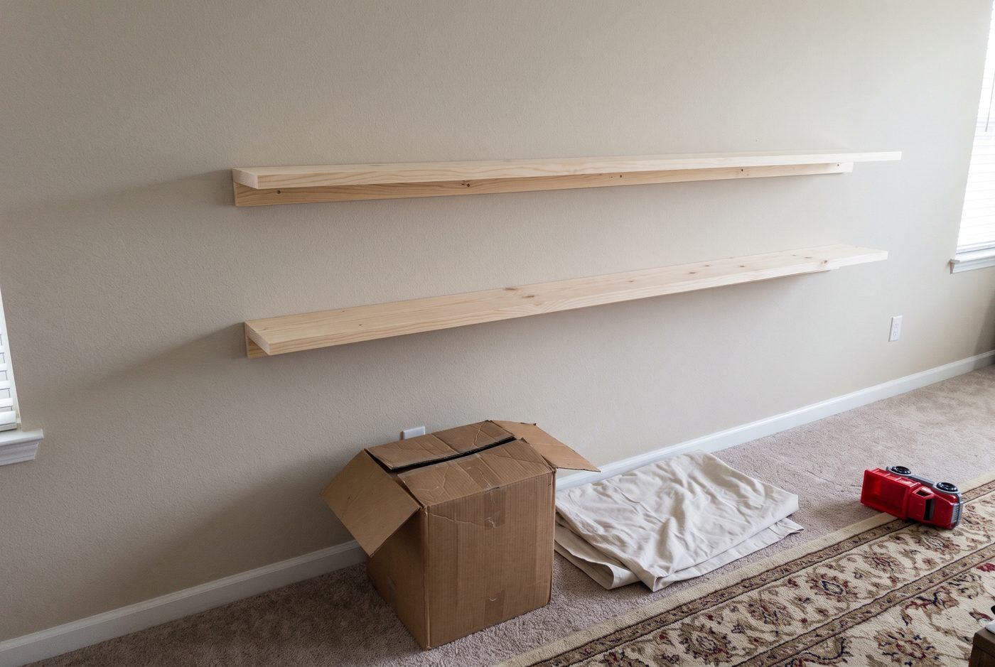Two empty wooden shelves mounted on a living room wall, box and dust sheet still on the floor